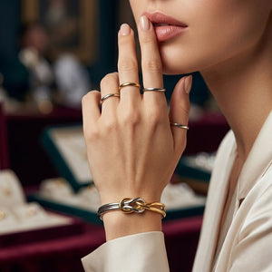 Woman wearing a two-tone gold and silver ribbon knot cuff with multiple rings in an upscale jewelry store setting