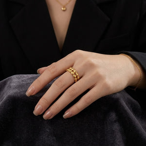Gold lattice link ring on a woman's hand, worn with a black outfit and a delicate gold bracelet.