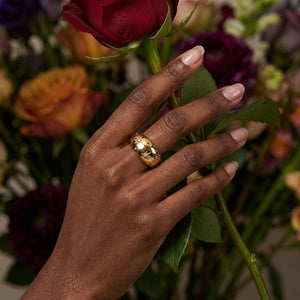 Gold starburst ring on hand, set against a background of colorful roses in a lifestyle context.