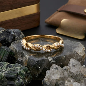 Gold spiral ring entwined with pearls, displayed on crystals with a leather pouch nearby.
