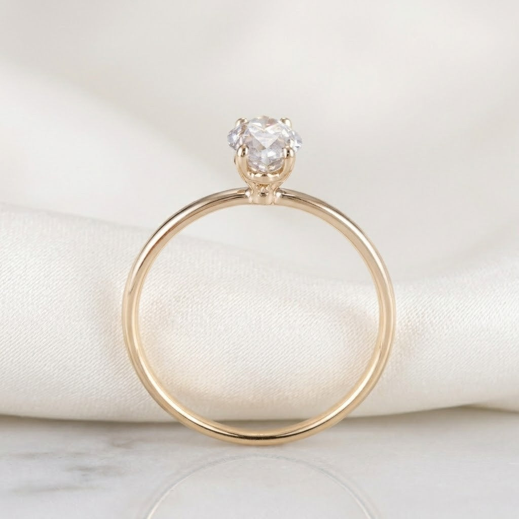 A gold solitaire engagement ring with a round brilliant-cut diamond, resting on a soft white satin fabric drape over a light marble surface - J.Collins Jewelry