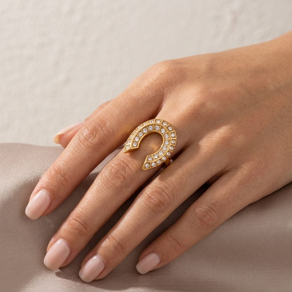 Gold horseshoe ring adorned with small gems on hand resting on fabric