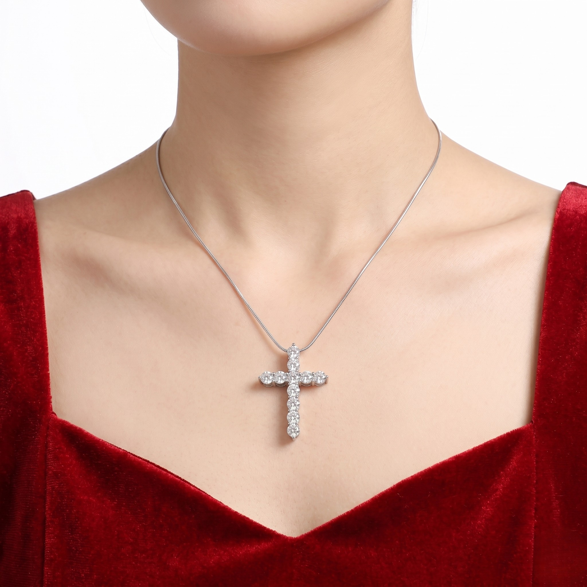 Elegant silver cross pendant with diamonds on a sleek chain, worn by a model in a red velvet dress.