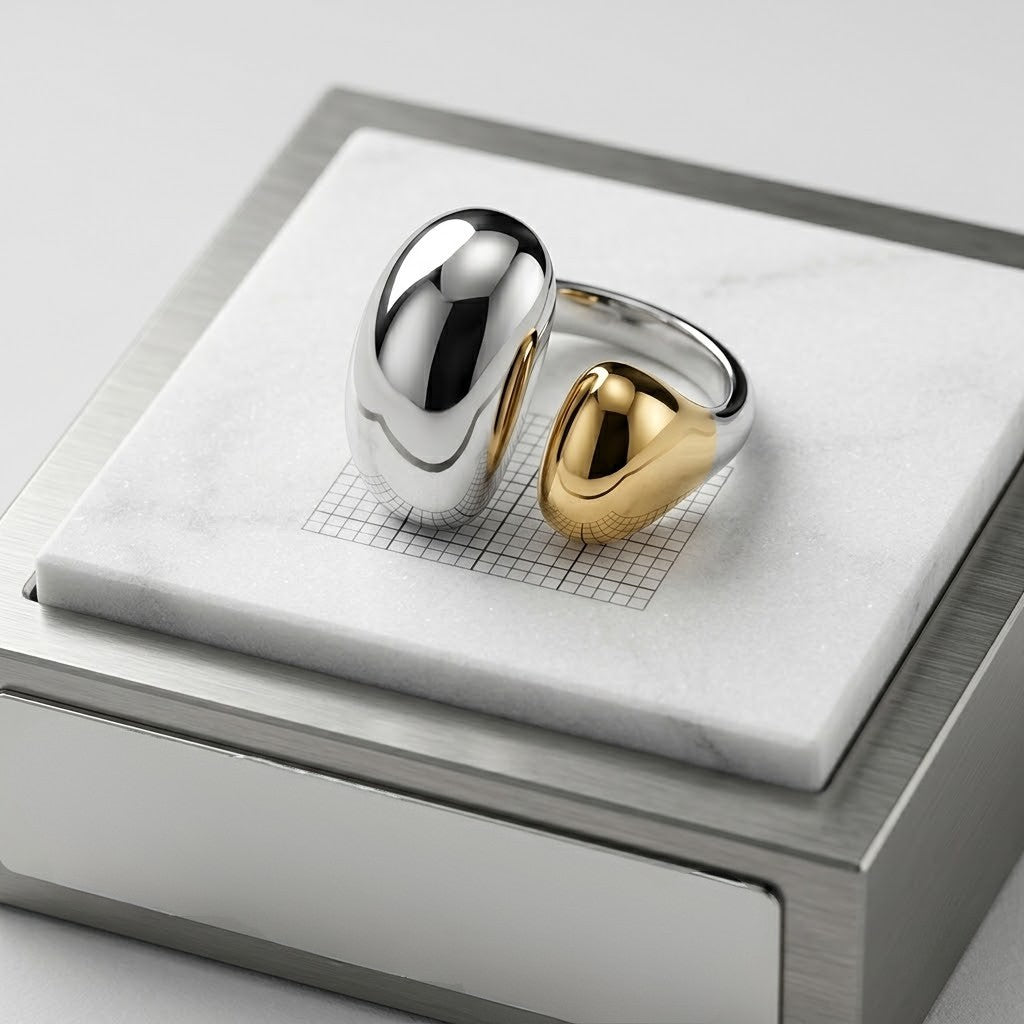 Silver and gold capsule ring with sleek design on a marble and stainless steel display.