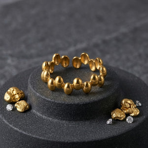 Oracle Beaded Ring in gold on display with gold nuggets and diamonds on a gray circular stand