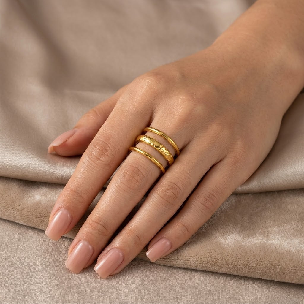 Gold Terra Triple Ring on hand with neutral manicured nails and beige fabric background