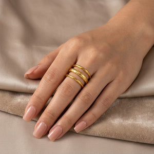 Gold Terra Triple Ring on hand with neutral manicured nails and beige fabric background