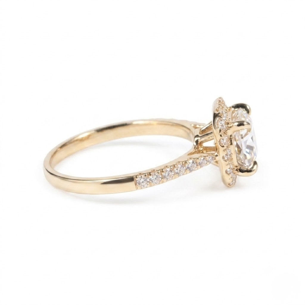 Gold ring featuring a cushion-cut cubic Moissanite center stone surrounded by a halo of round accents shown in a side profile view on a plain white background by J.Collins
