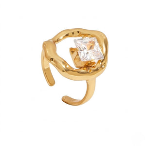 Gold ring with fluid design and a large square-cut clear gemstone centerpiece