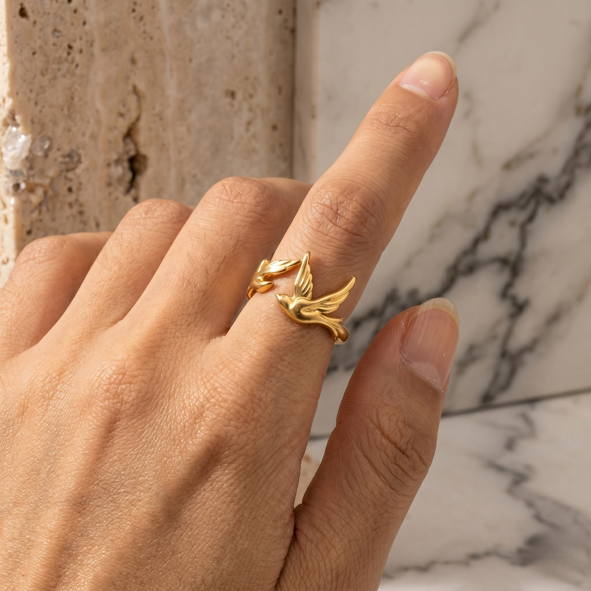 Gold ring with foliage design on model's finger against marble background