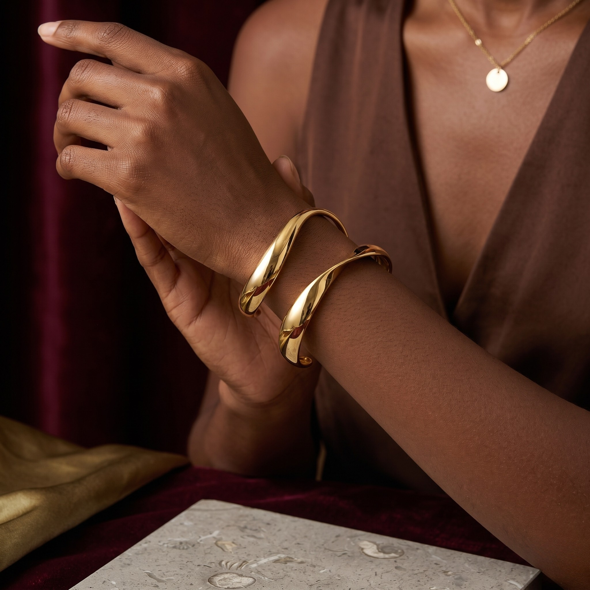 Gold Infinity Curve Bangles on model's wrist, elegant lifestyle setting, paired with a pendant necklace