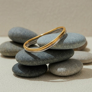 Bi-Color Arc Bracelet with gold and silver bands displayed on smooth gray stones