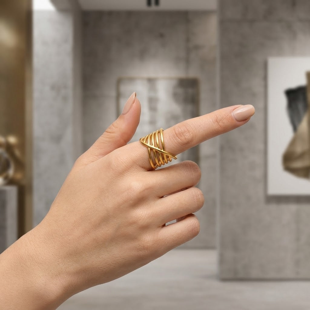 Gold wave crossover ring displayed on a hand, set in a modern gallery background.