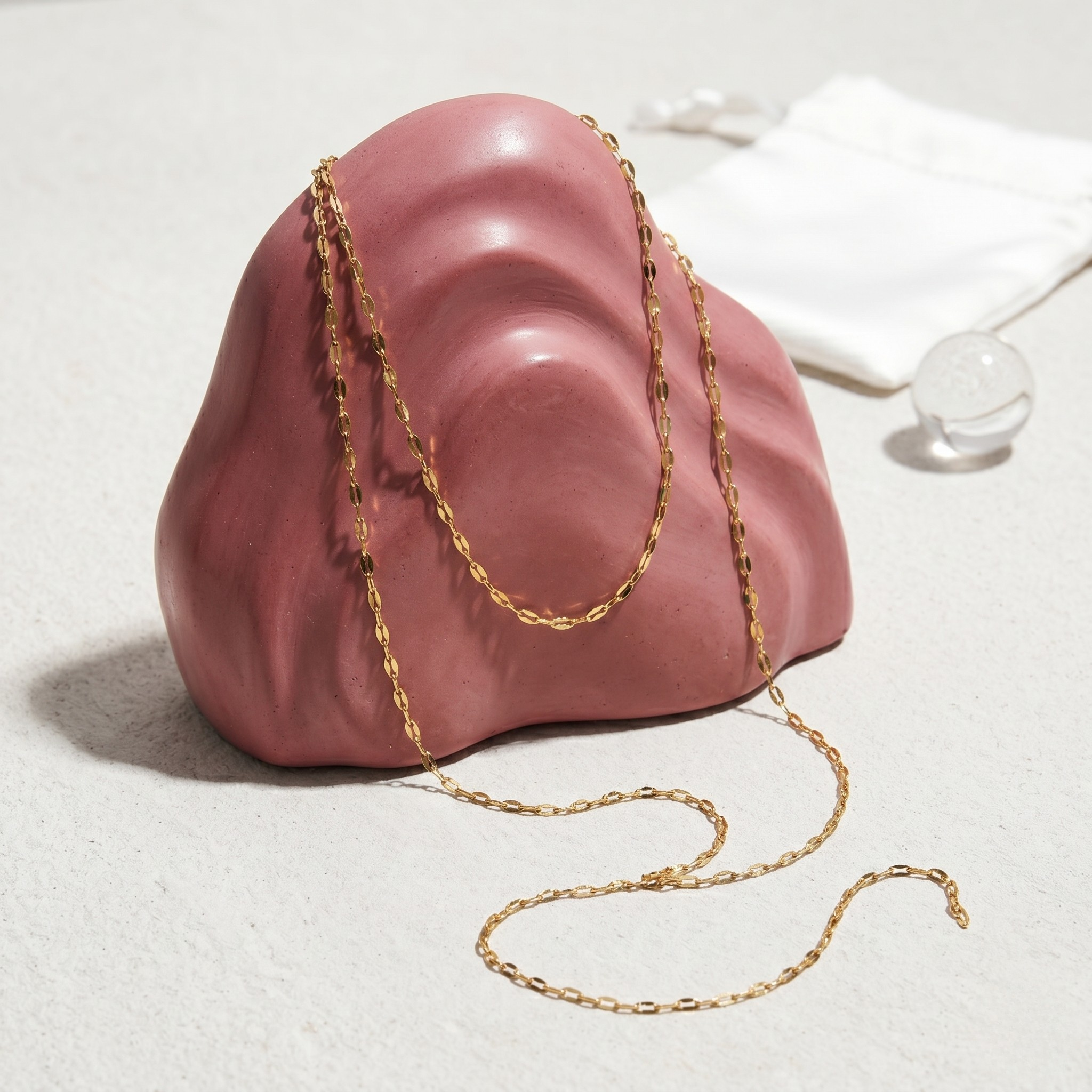 Gold Y-Link Chain displayed on a pink sculptural stand in a minimalist setting
