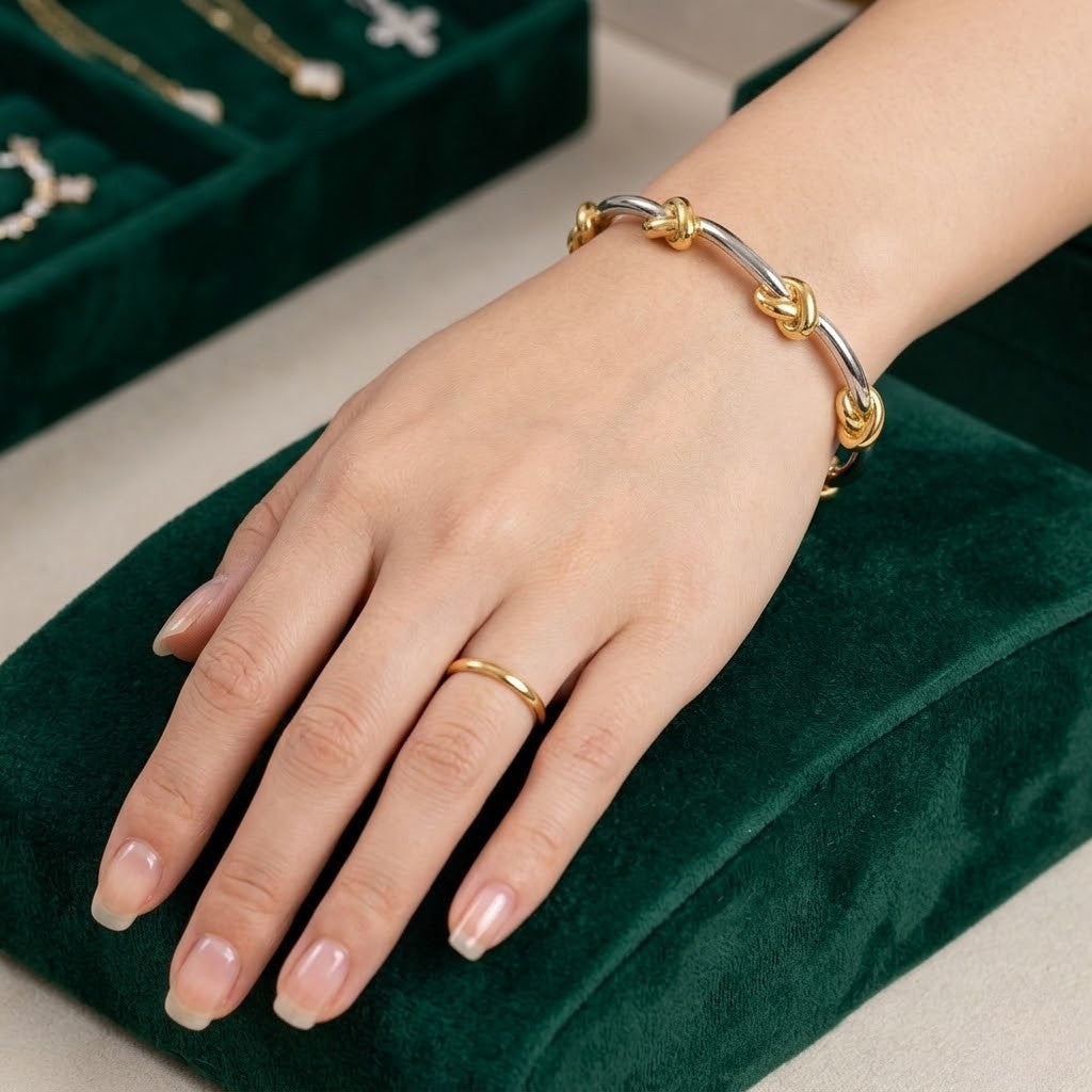 Woman's hand wearing gold and silver knot bangle with green velvet background and jewelry display.