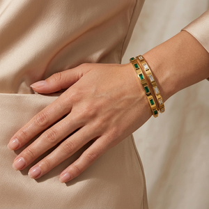 Emerald and gold bangle set on woman's wrist, elegant attire, showcasing jewelry style and luxury fashion.