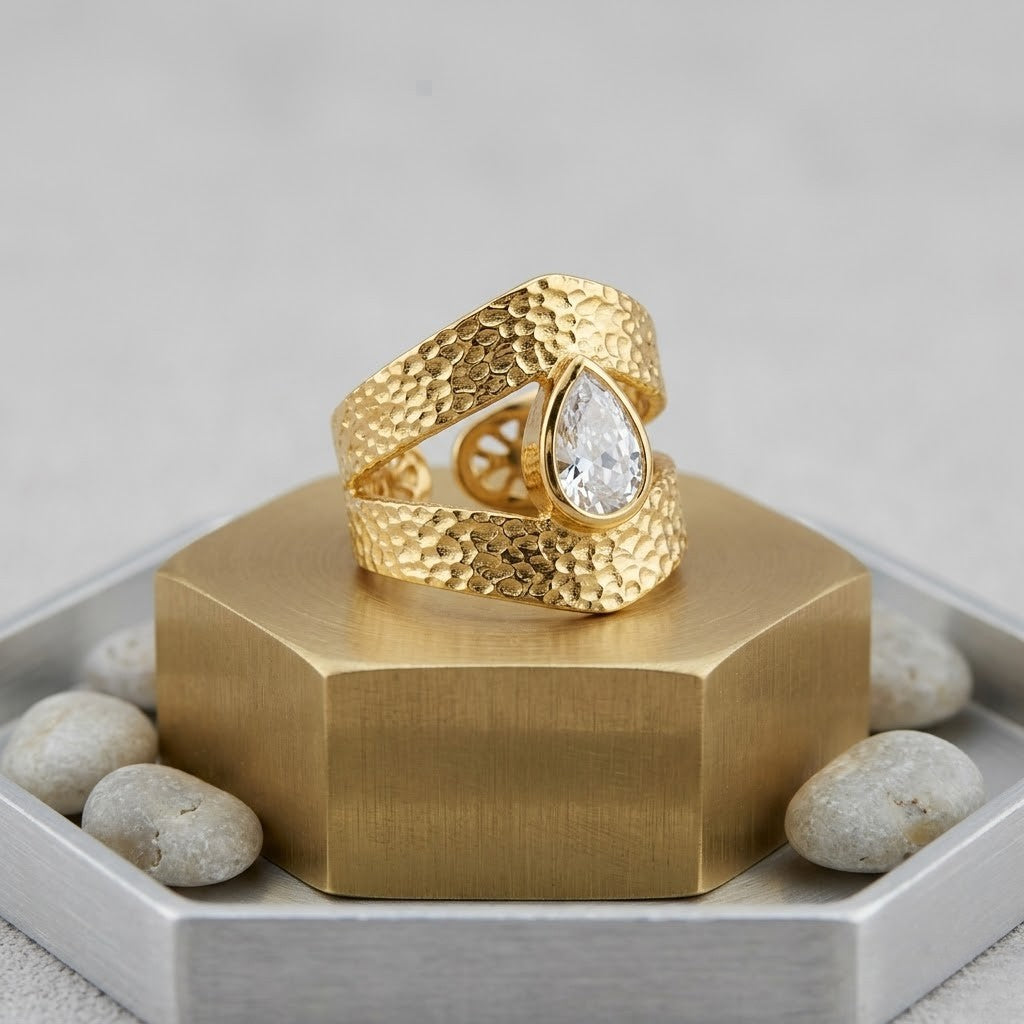 Gold teardrop ring with textured band, set on a hexagonal stand with accent stones