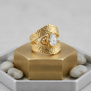 Gold teardrop ring with textured band, set on a hexagonal stand with accent stones