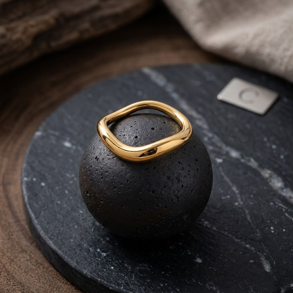 Gold wave band ring on black stone display, J.Collins Jewelry