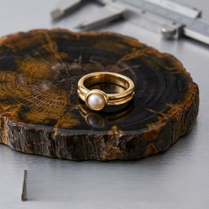 Gold ring with pearl inset on decorative wooden base, calipers in background