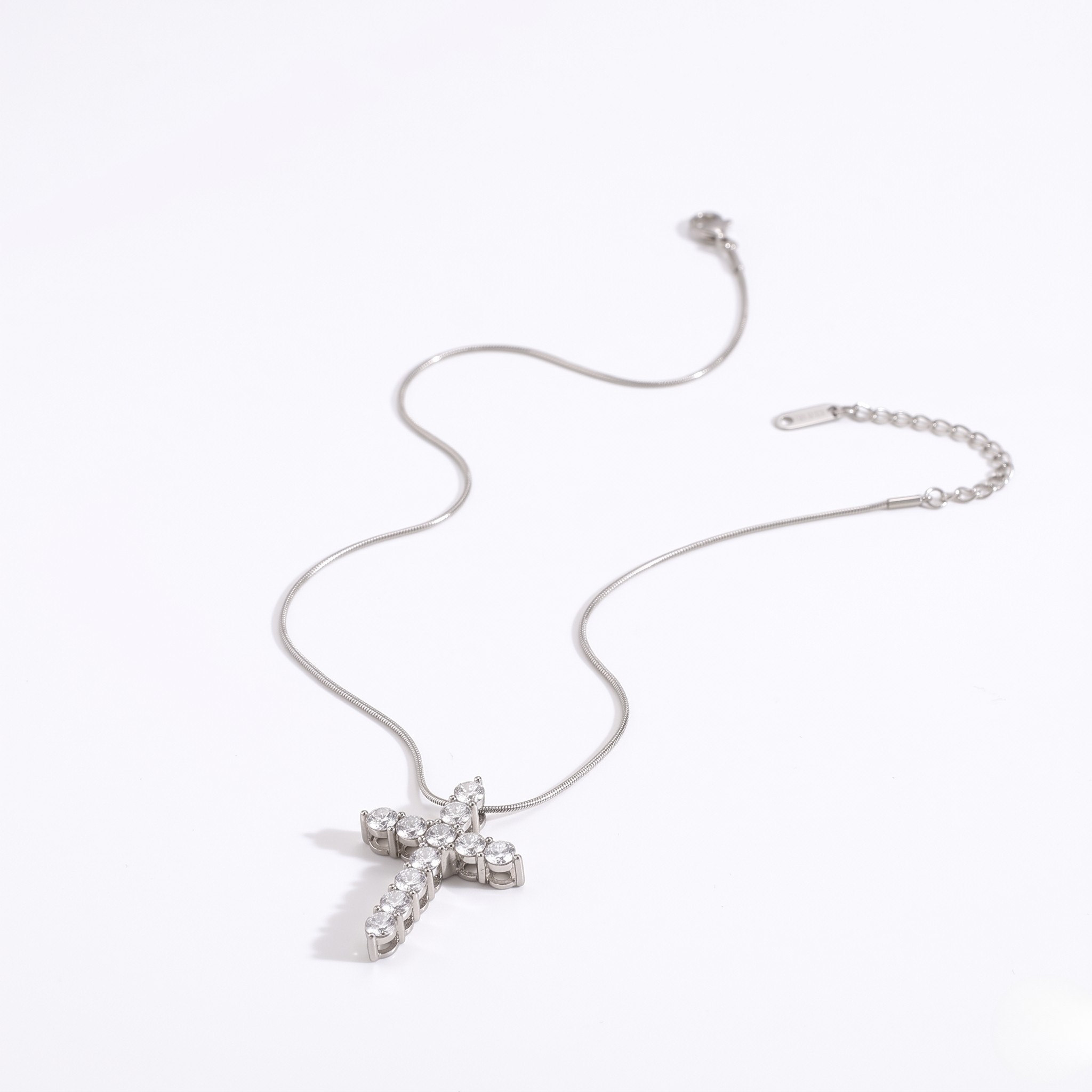 Silver cross necklace with clear gemstones on a delicate chain, featuring adjustable clasp.