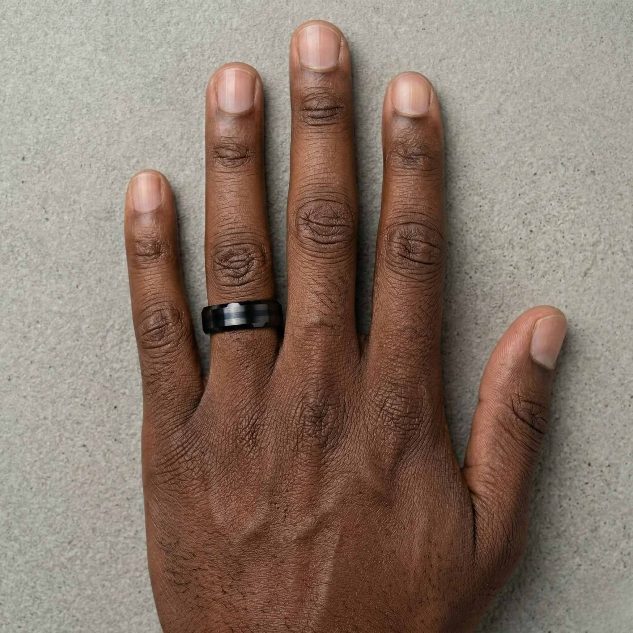 Hand wearing a black ring on a gray background