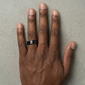 Hand wearing a black ring on a gray background