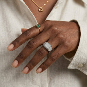 Silver Alpha Crest Ring with pavé diamonds on a model's hand, alongside an emerald gold ring and necklace.