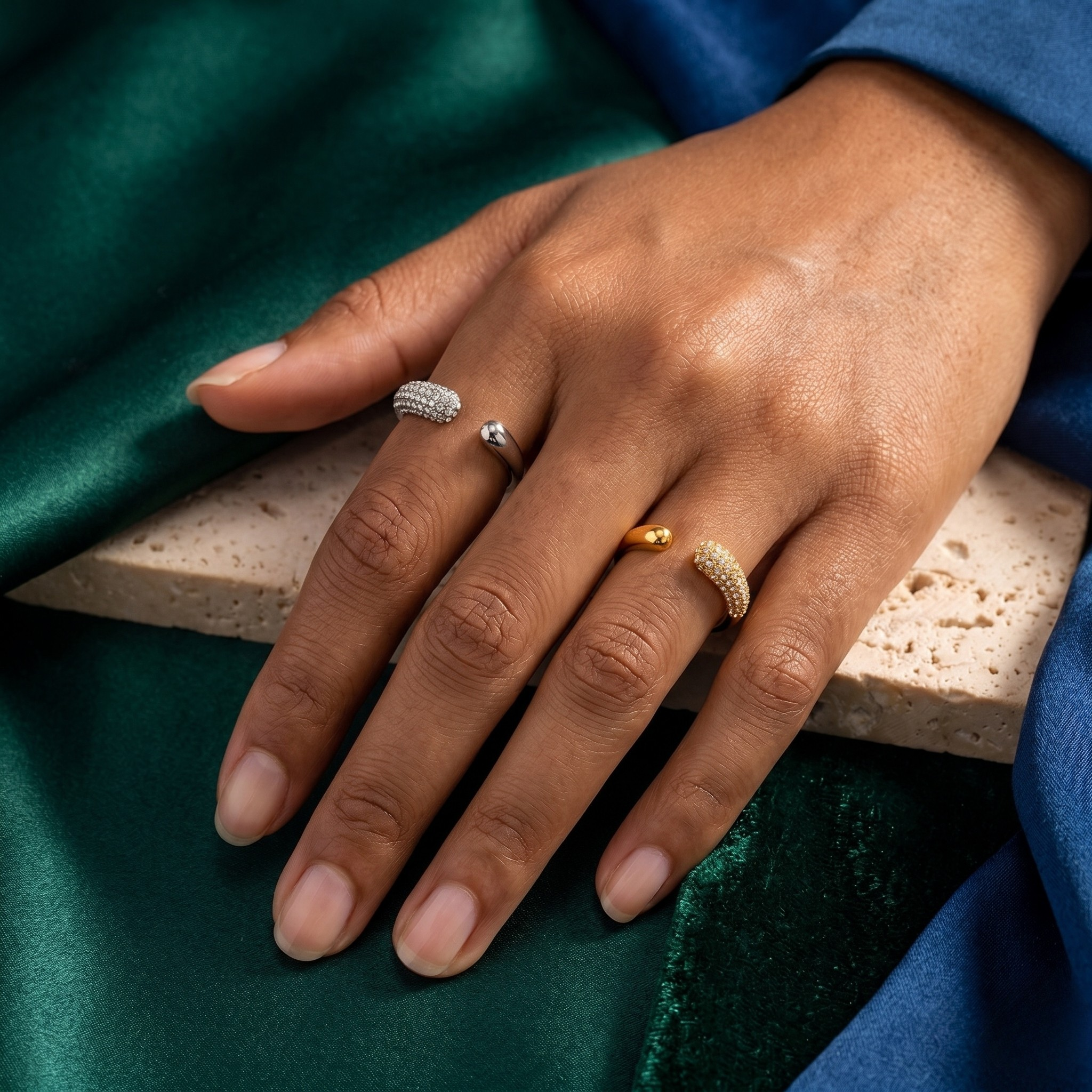 Hand wearing gold and silver curved pavé rings on green velvet background