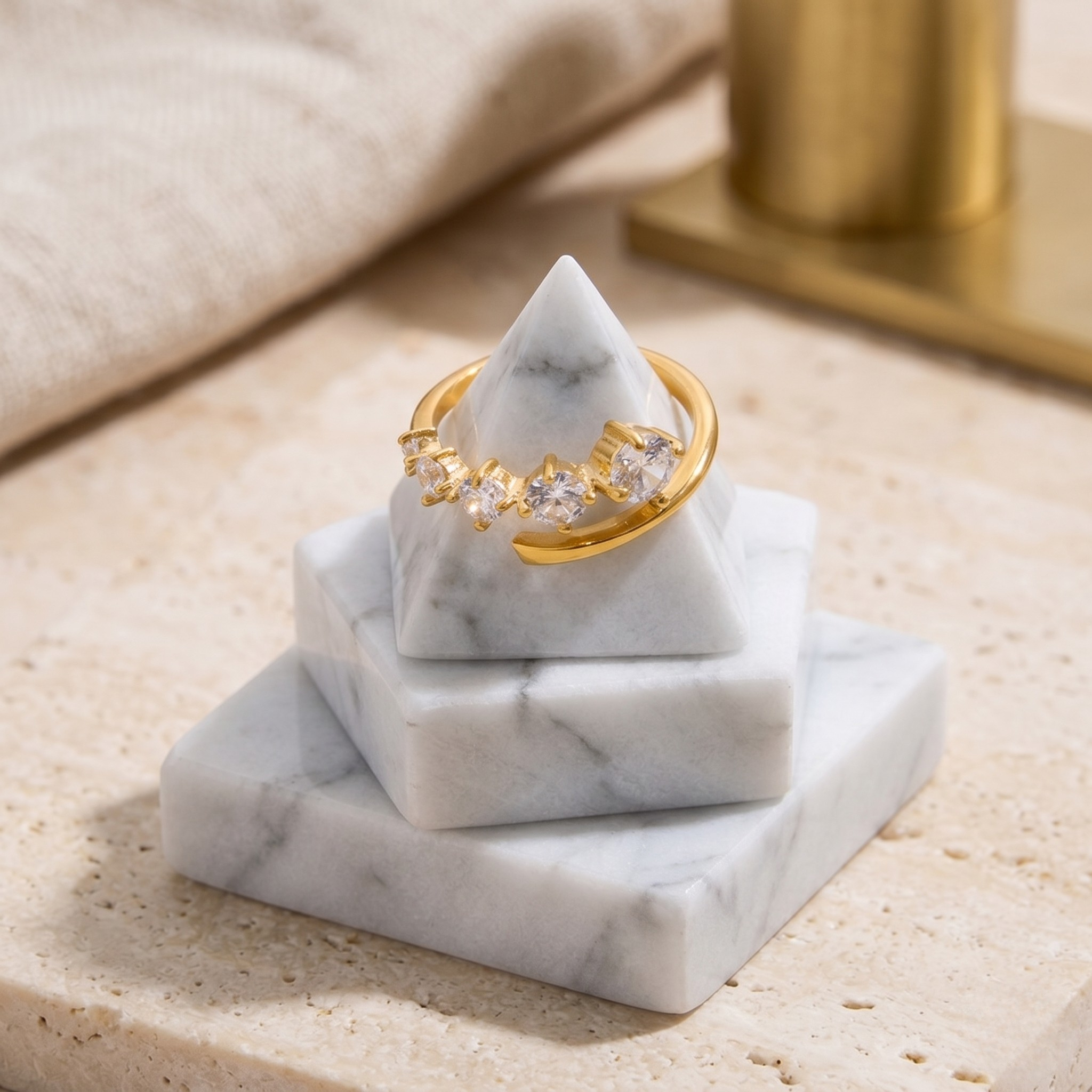Gold prongs ring with clear gemstones on a marble pyramid display stand