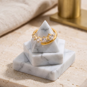 Gold prongs ring with clear gemstones on a marble pyramid display stand