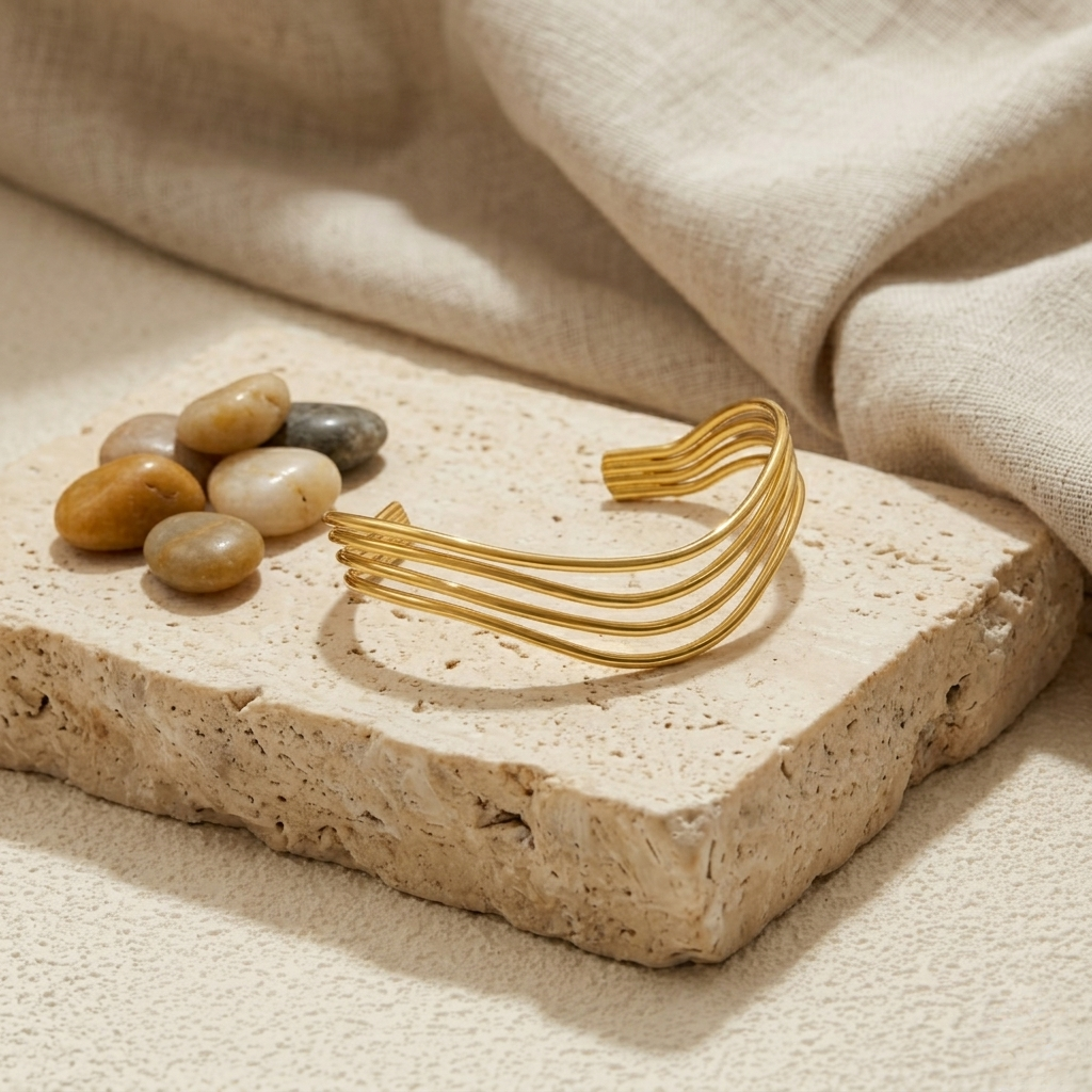 Layered hollow gold bangle on stone slab with pebbles and linen fabric background