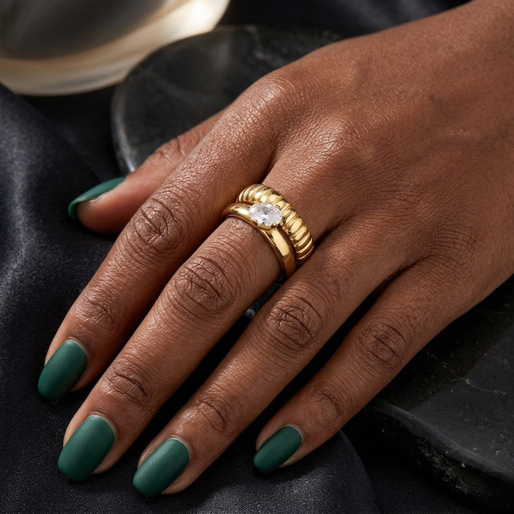 Gold twist ring with a central gemstone worn on a model's hand with green nail polish.