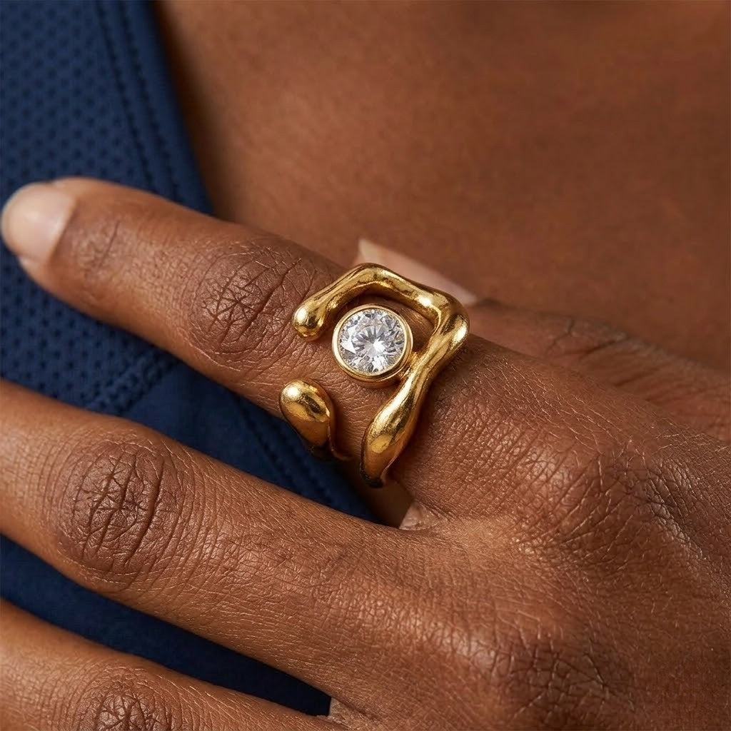 Gold kinetic ring with a round crystal on a hand, featuring a fluid, organic design and worn by a person.