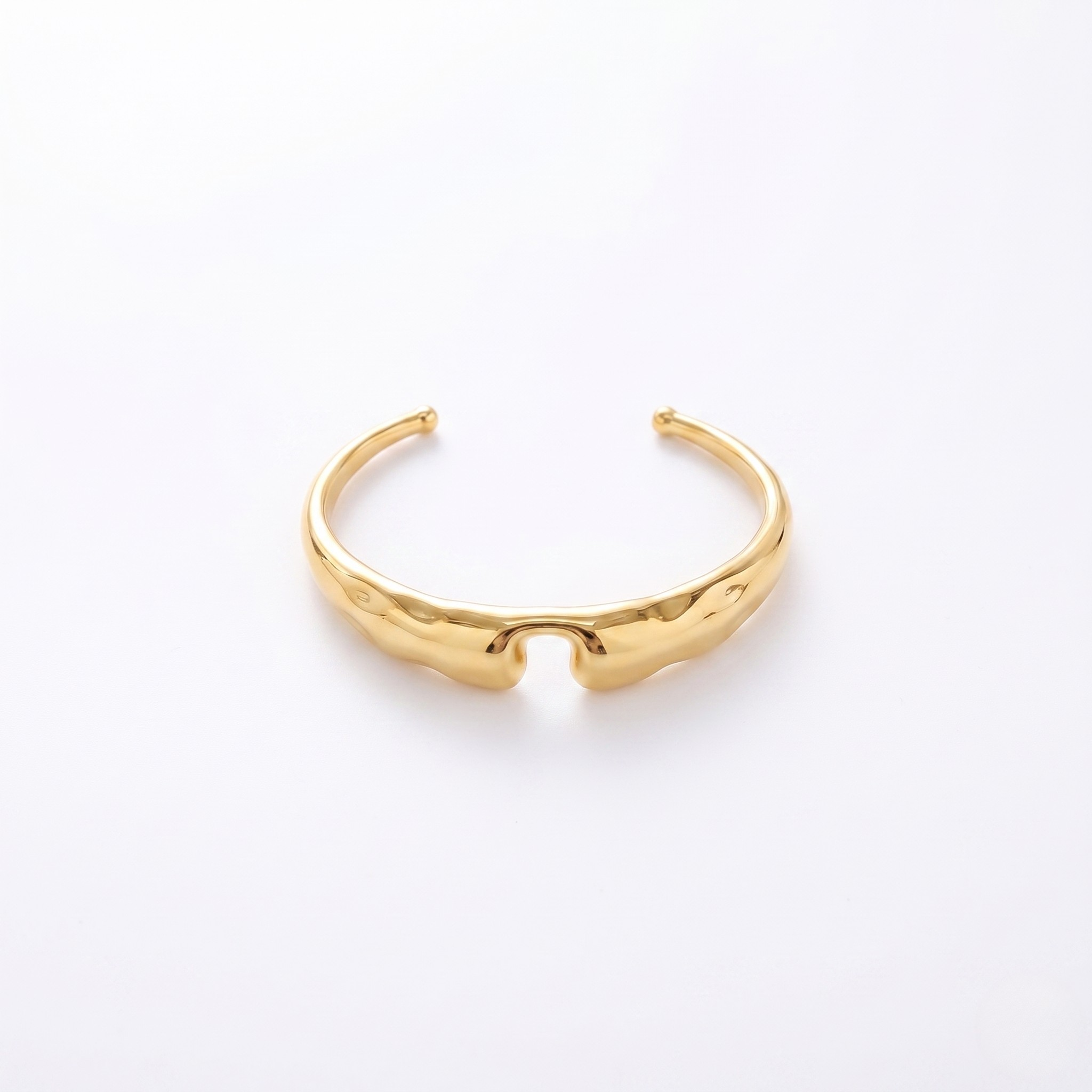 Bold sculpted gold cuff with open ends and a sleek, textured design on a white background