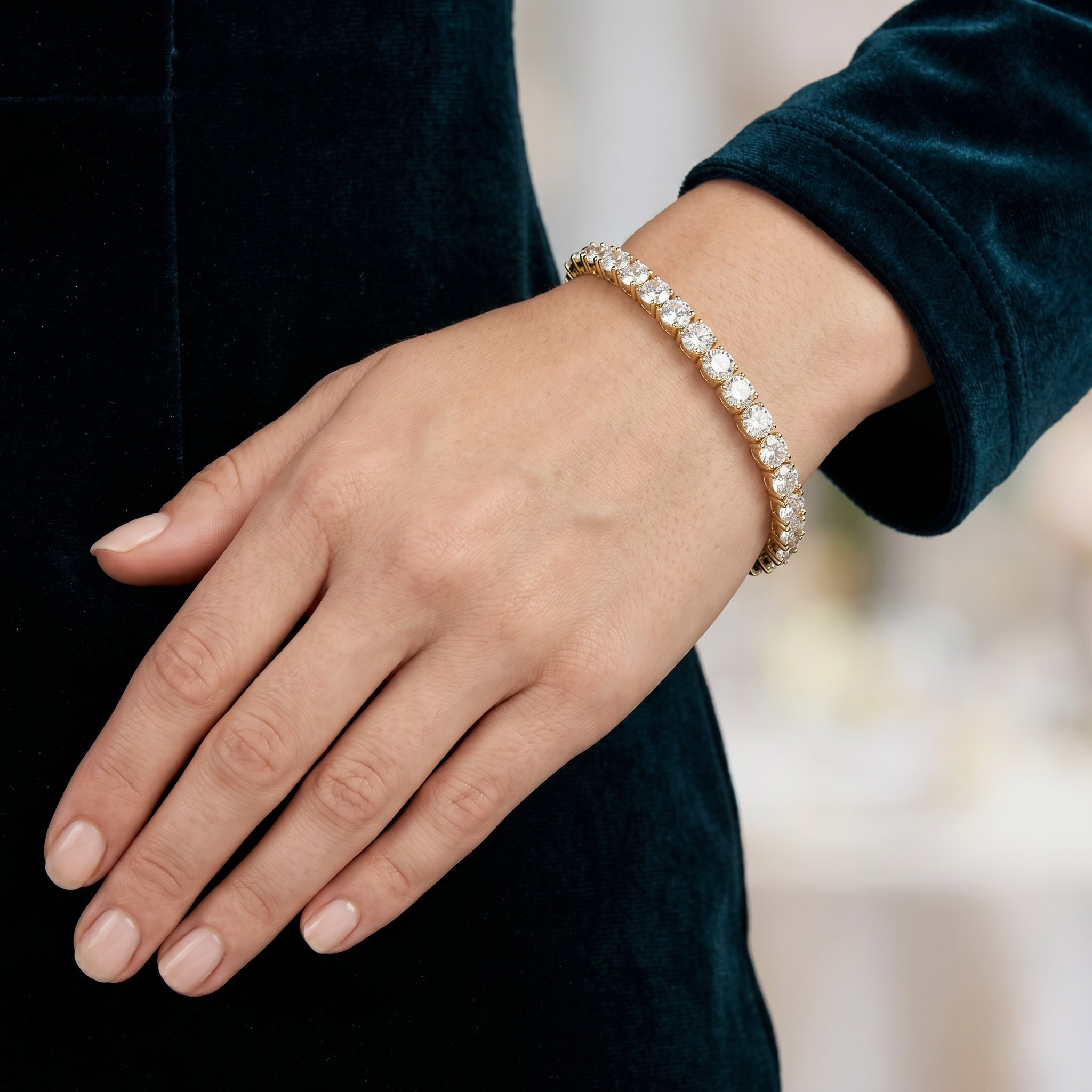 Woman's hand wearing gold classic tennis bracelet with 5mm round diamonds against a dark velvet dress backdrop