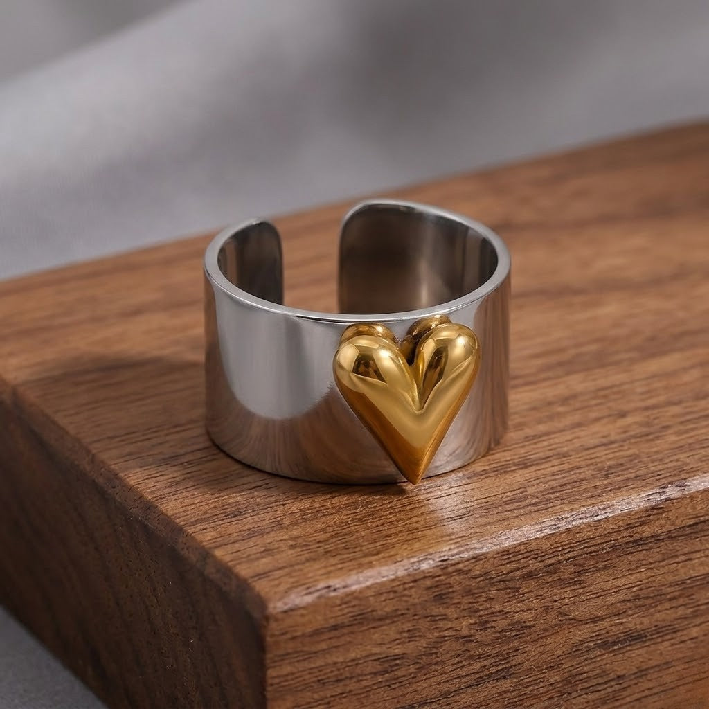 Silver band ring with gold heart accent displayed on a wooden surface