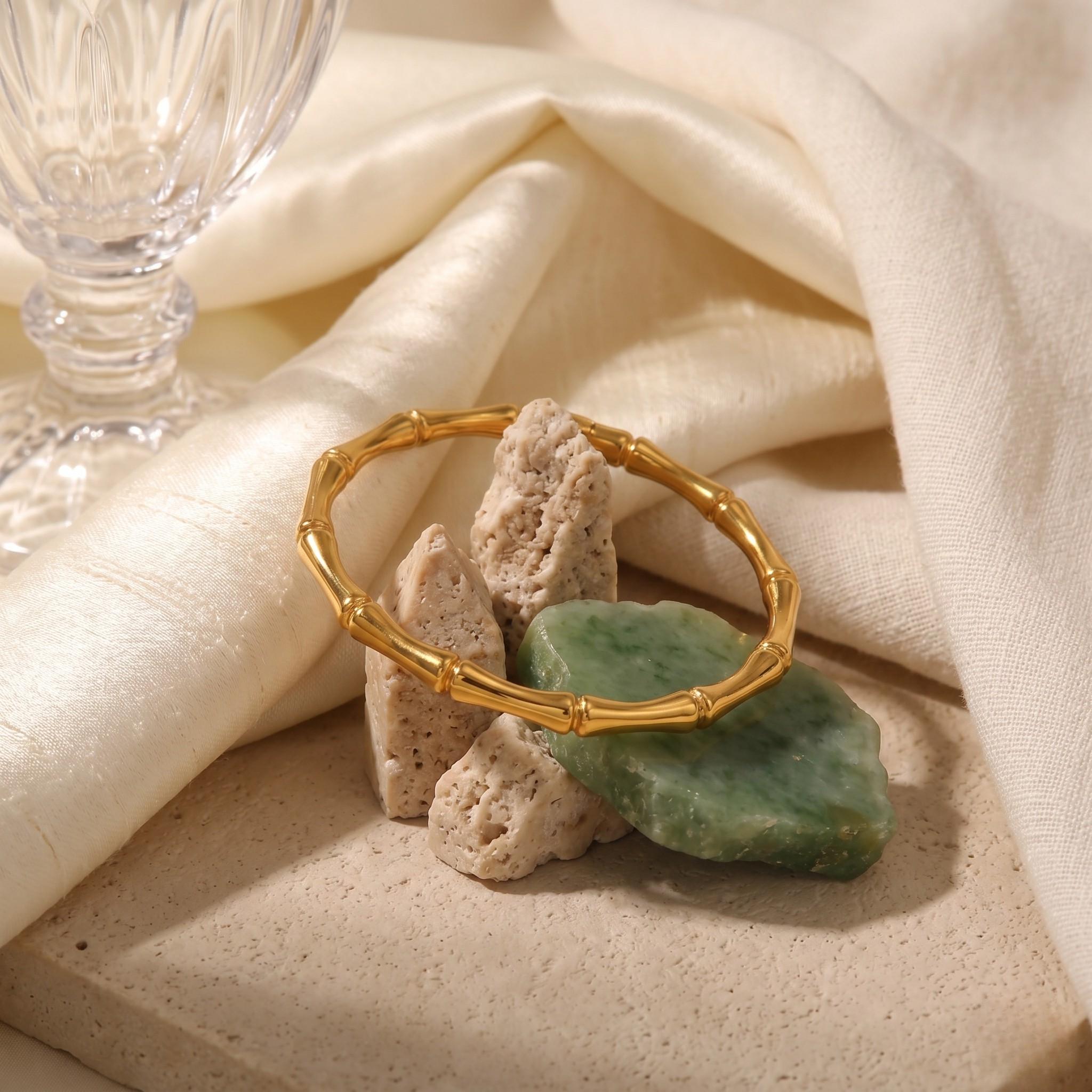 Sculpted Bamboo Bracelet in gold on fabric with greenery and stone background, elegant lifestyle display.