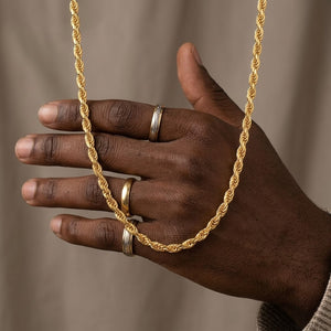 Detailed view of a classic gold rope chain draped across a hand wearing textured gold bands | J.Collins Jewelry