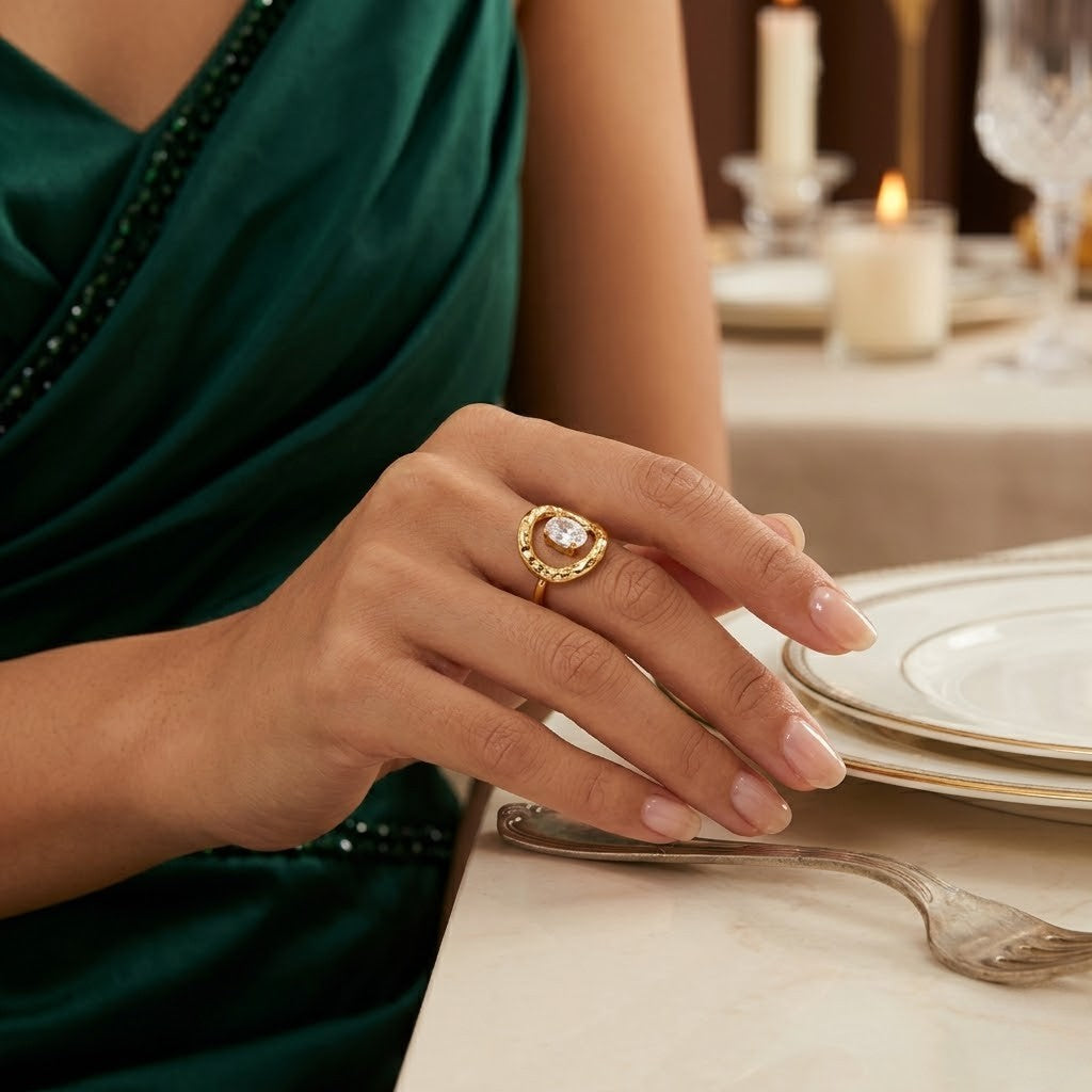Gold organic crown ring with central stone on woman's hand at a dining table, dressed in an elegant green gown.