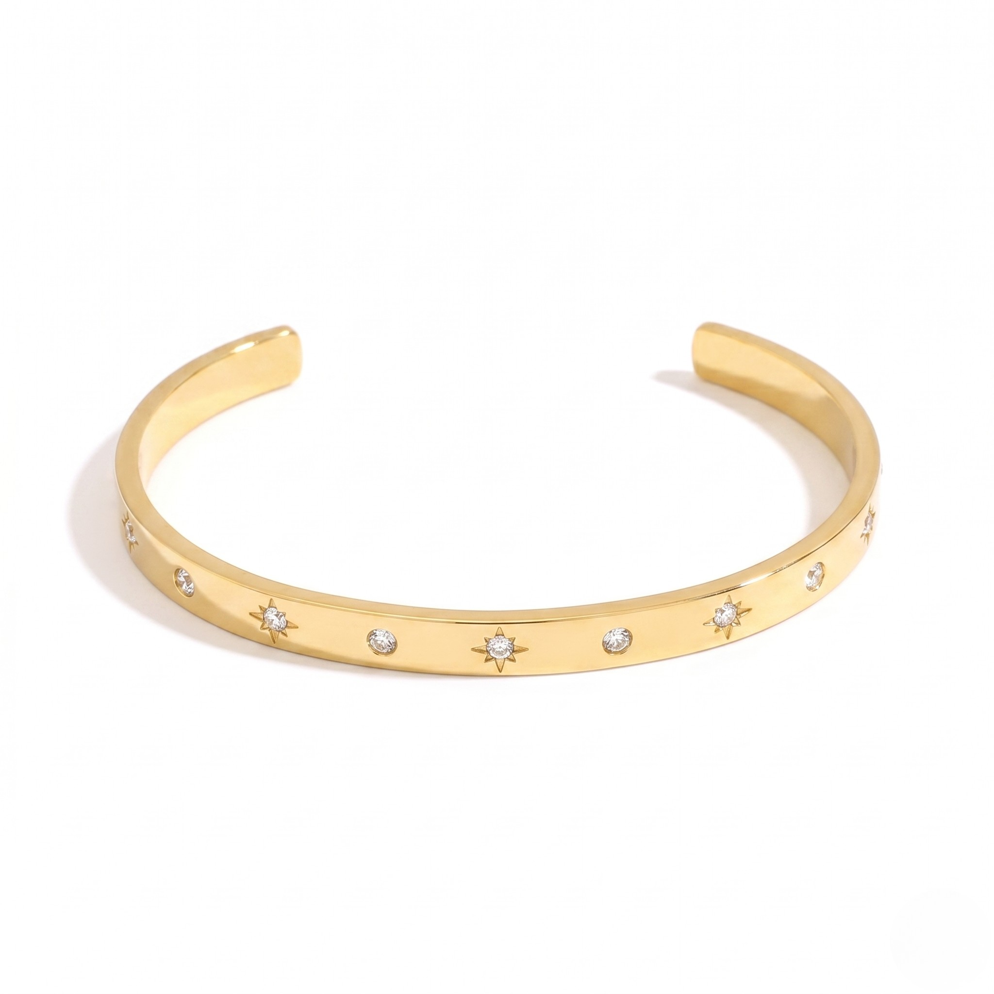 Gold cuff bracelet with starburst engravings and small diamonds on a plain white background