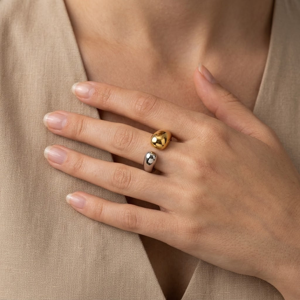 Hand wearing a gold and silver bi-tone steel ring, contrasting finish, neutral fabric background