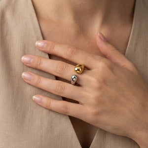 Hand wearing a gold and silver bi-tone steel ring, contrasting finish, neutral fabric background