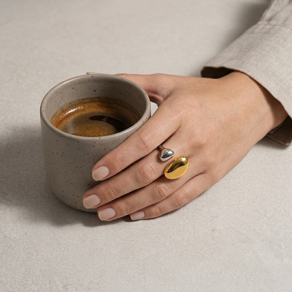 Hand wearing silver and gold Luxe Steel Ring holding a matte ceramic coffee cup on a light stone surface
