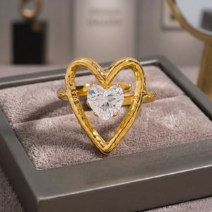 Heart-shaped gold ring with a clear stone accent, displayed on a fabric-lined jewelry box.