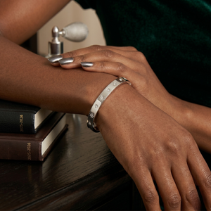 Silver starburst engraved cuff worn on wrist with dark green velvet background and books nearby.