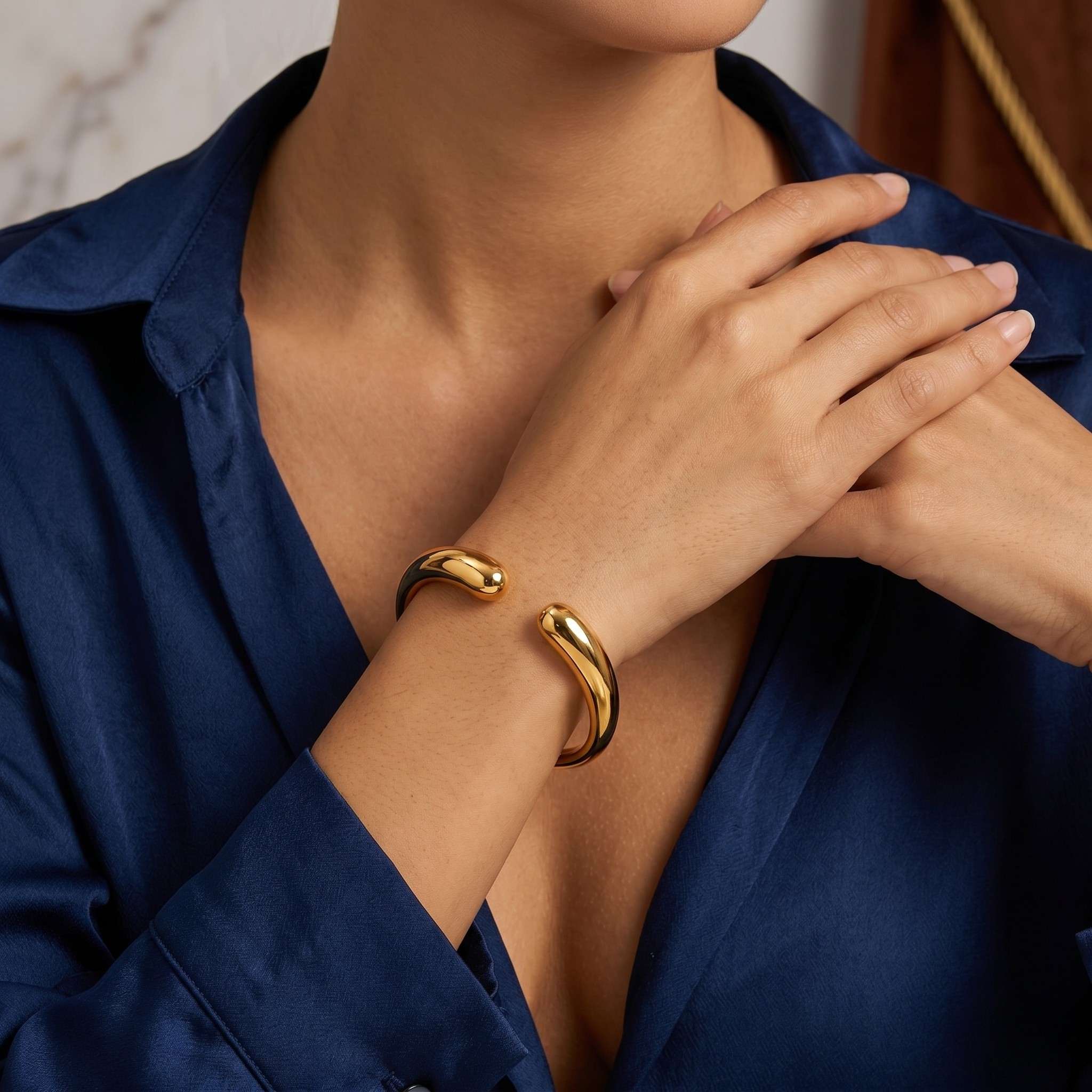 Gold cuff bracelet on a model's wrist, styled with a blue shirt, showcasing elegant, minimalist design.