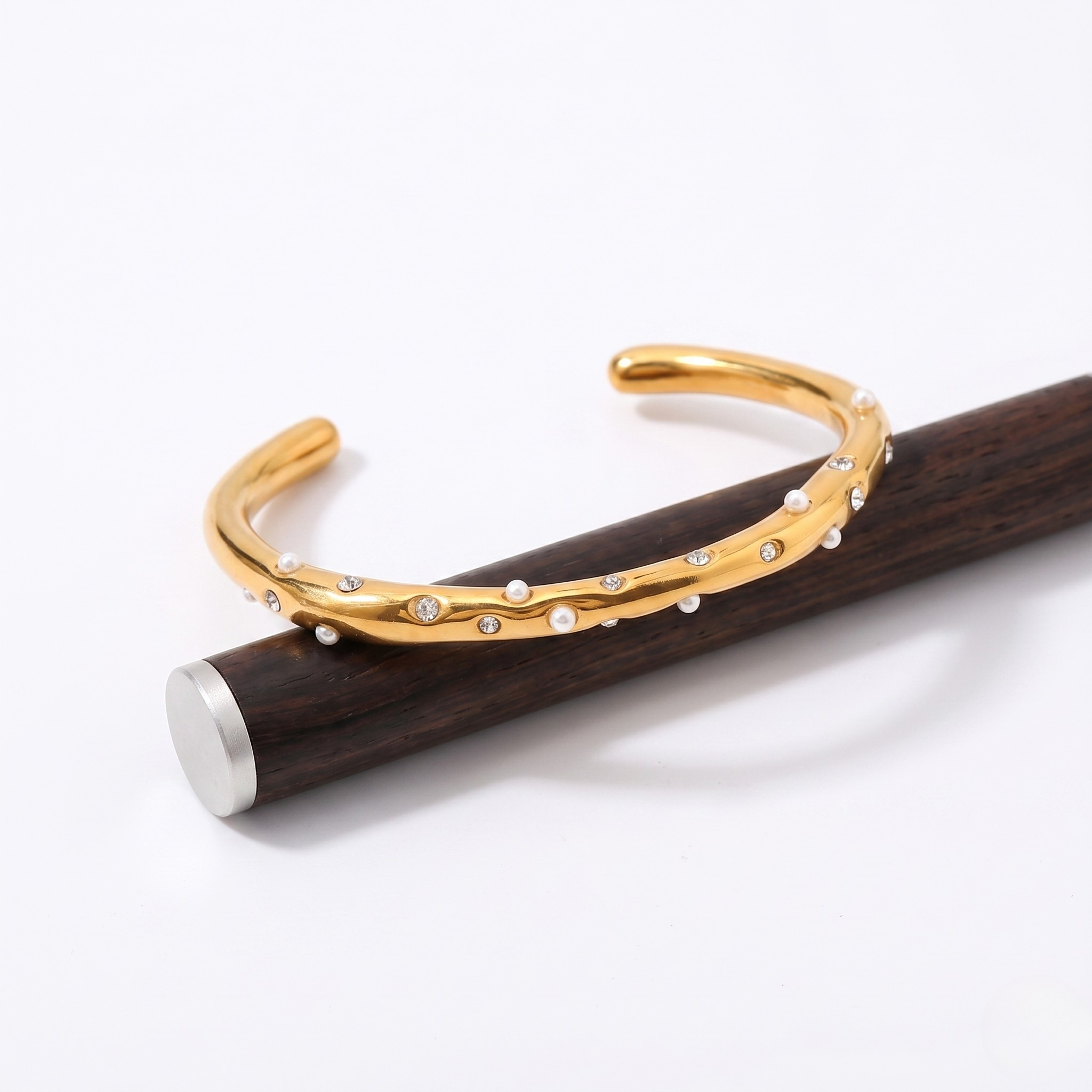 Gold cuff bracelet with diamond accents and a branch-like design on a wooden display stand