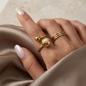 Gold pearl sphere ring worn on hand against satin fabric backdrop