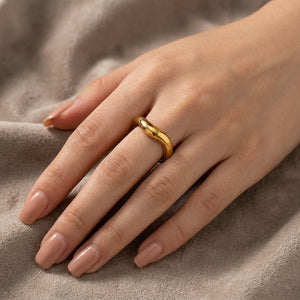 Gold wave band ring on female hand with neutral manicure resting on soft fabric